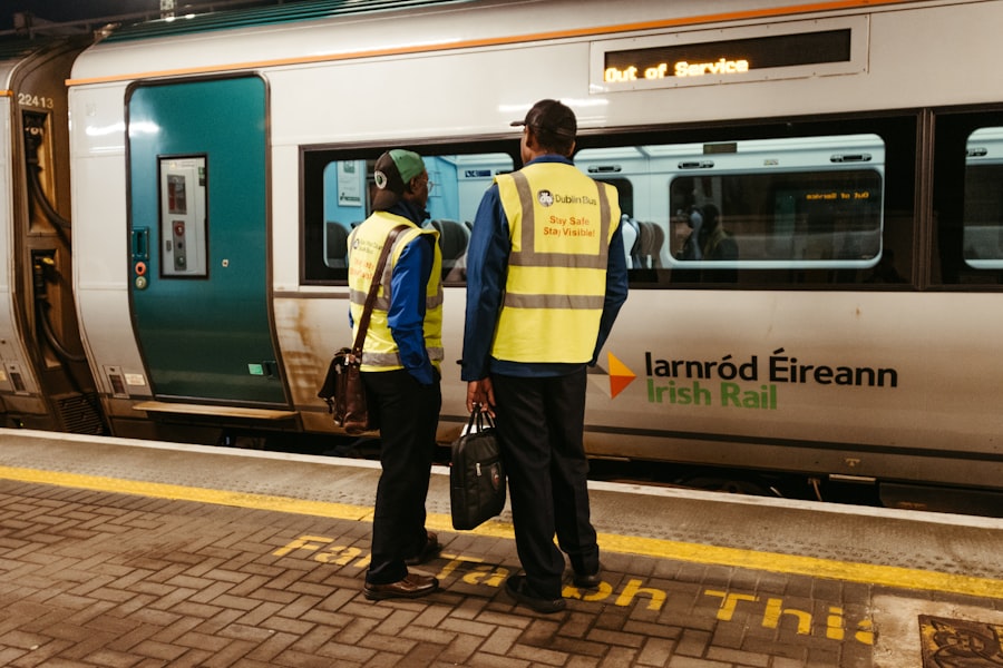 Two workers in high-visibility vests stand by a train.